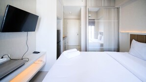 A hotel room with a bed, a TV mounted on the wall, a bedside table, and a mirror. - Nice Studio Connected To Mall At Tanglin Supermall Mansion Apartment (Surabaya)