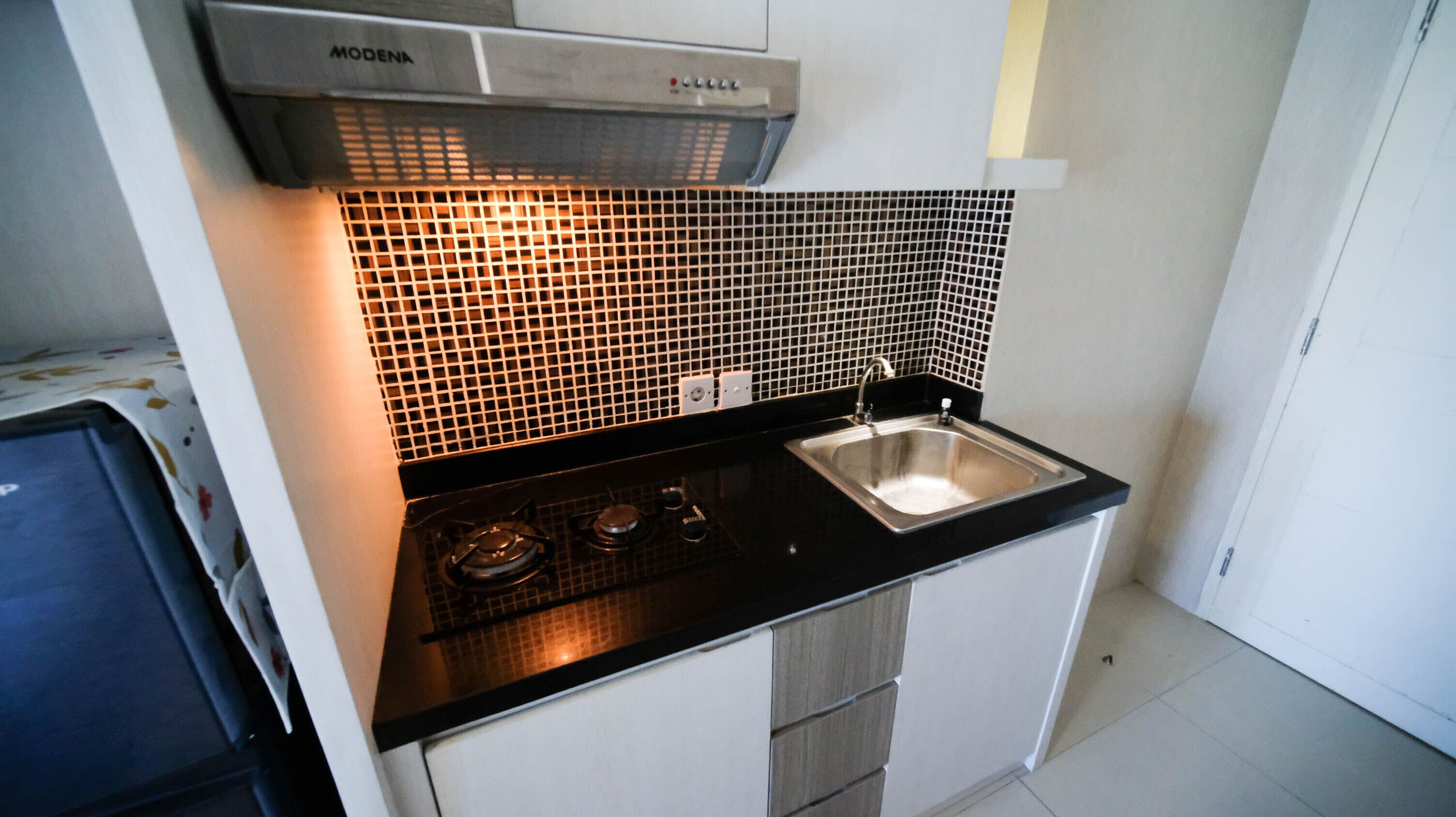 A compact kitchen with a black countertop, a stainless steel sink, a gas stove, and a black tiled backsplash.