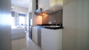 A compact kitchen with a gas stove, a sink, and a microwave. There is a window with curtains and a bed in the adjacent room. - Nice Studio Connected To Mall At Tanglin Supermall Mansion Apartment (Surabaya)