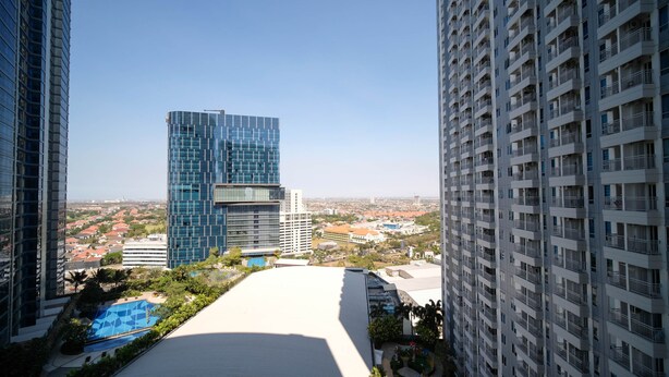 A high-rise building with a modern glass facade, surrounded by other high-rise buildings and a residential area with houses in the background. - Nice Studio Connected To Mall At Tanglin Supermall Mansion Apartment (Surabaya)