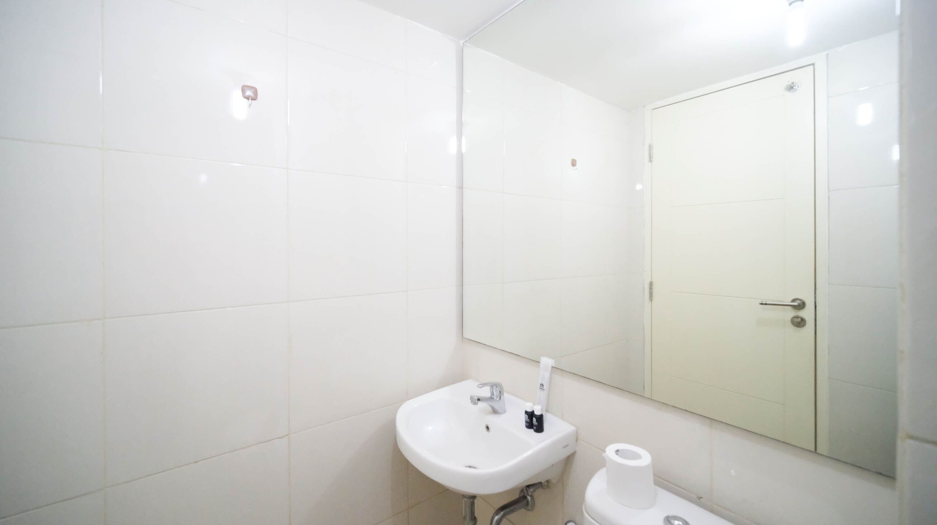 A bathroom with white tiles, a sink, a toilet, and a mirror.