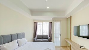 Quarto de hotel com uma cama grande, um sofá cinzento, uma TV fixada na parede e uma porta de vidro deslizante que dá para uma varanda.