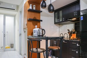 A compact kitchen with a black countertop, two bar stools, a coffee maker, and a black refrigerator. - Warm And Homey 2Br At Sentraland Cengkareng Apartment (Jakarta)