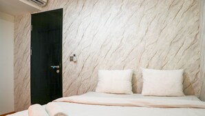 A hotel room with a marble-patterned wall, a black door, two white pillows, and a neatly made bed with rolled towels. - Warm And Homey 2Br At Sentraland Cengkareng Apartment (Jakarta)