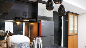 A modern kitchen with dark cabinets, a stainless steel refrigerator, a kettle, and a marble countertop. - Warm And Homey 2Br At Sentraland Cengkareng Apartment (Jakarta)