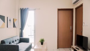 A living room with a sofa, a TV on a stand, a small table with a plant, and a door. - Comfort Designed 2Br Apartment At Mediterania Palace Residence (Jakarta)