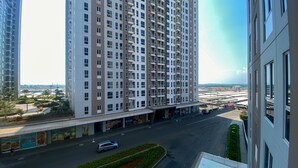 A high-rise residential building with multiple balconies, a parking area, and a commercial building with food advertisements. - Homey Living Studio Room At Tokyo Riverside Pik 2 Apartment (Teluknaga)