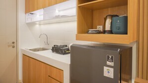 A compact kitchen with wooden cabinets, a stainless steel sink, a built-in stove, and a refrigerator. - Homey Living Studio Room At Tokyo Riverside Pik 2 Apartment (Teluknaga)