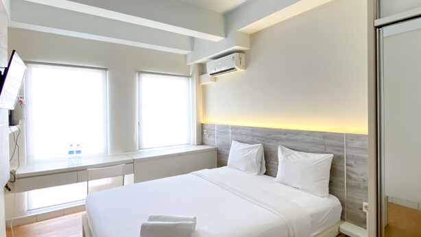 A modern hotel room with a large bed, built-in desk, and a view of the city. - Modern Look And Comfy Studio Patraland Urbano Apartment (Bekasi)