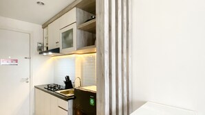 A compact kitchen with white cabinets, a microwave, a sink, and a refrigerator. - Modern Look And Comfy Studio Patraland Urbano Apartment (Bekasi)