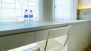A modern kitchen with a white countertop, a white chair, and two Oasis water bottles on the window sill. - Modern Look And Comfy Studio Patraland Urbano Apartment (Bekasi)