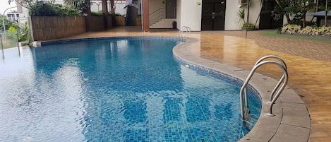 A swimming pool with a tiled edge, a metal handrail, and a building with a balcony in the background.