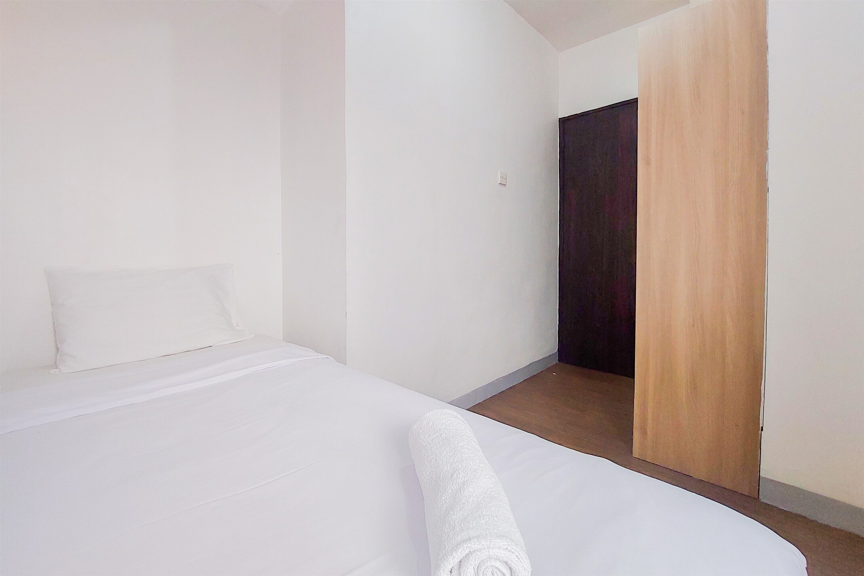 A clean, minimalist hotel room with a neatly made bed, a wooden door, and white walls.