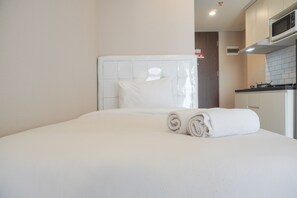 A hotel room with a neatly made bed, a white headboard, and a small kitchenette area. - Wonderful And Homey Studio Vasaka Solterra Apartment (Jakarta)
