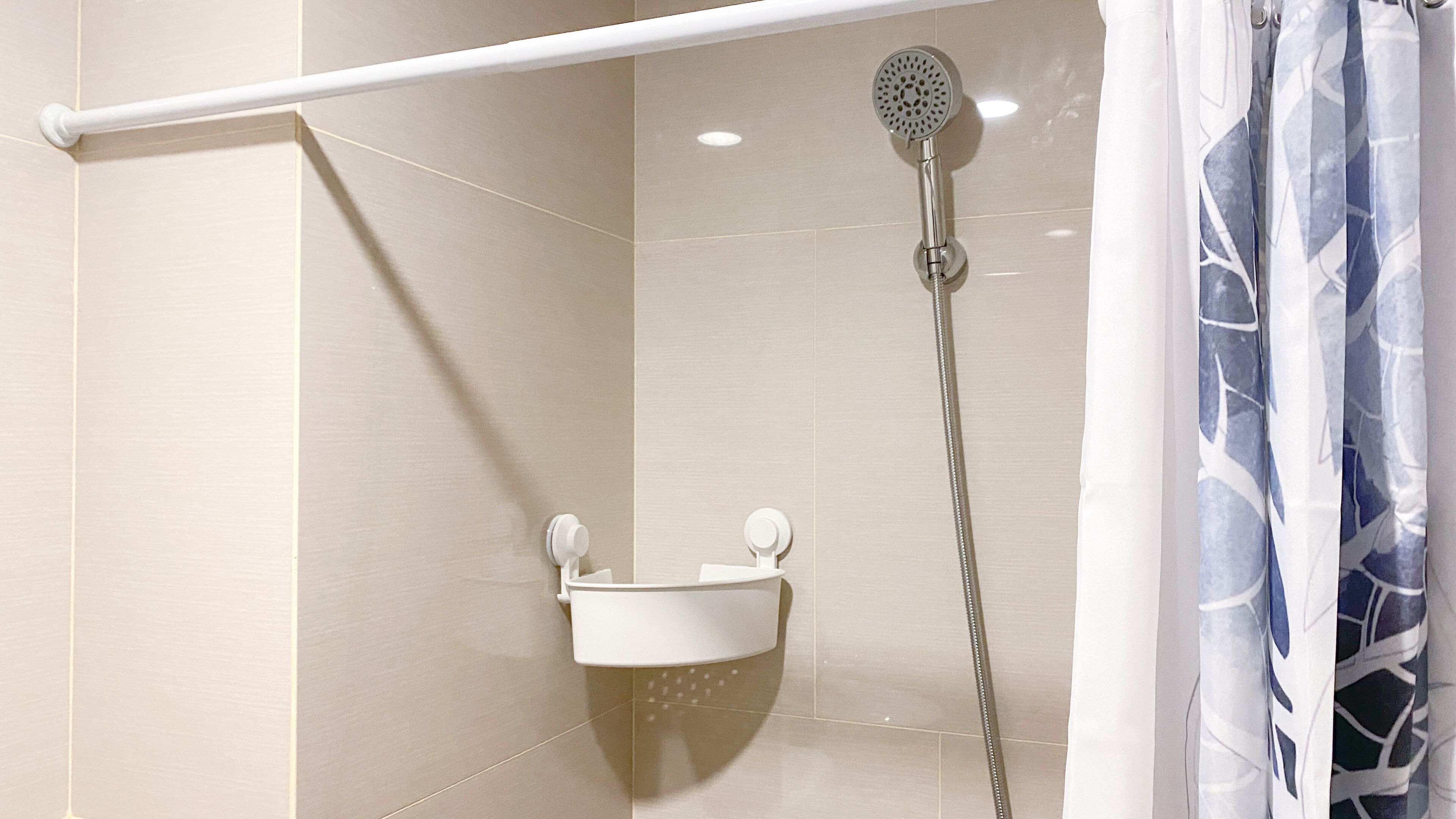Área de chuveiro com chuveiro manual, pia fixada na parede e porta-toalhas.