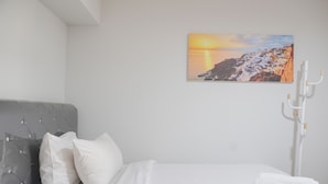 Un dormitorio con cama, almohadas blancas, una colcha blanca, una toalla blanca y un radiador fijado a la pared.