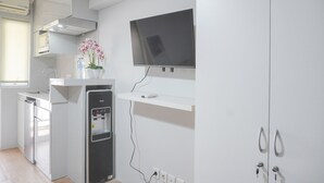 Una cocina moderna con refrigerador empotrado, dispensador de agua, televisor de pantalla plana montado en la pared y una pequeña repisa sobre el refrigerador.