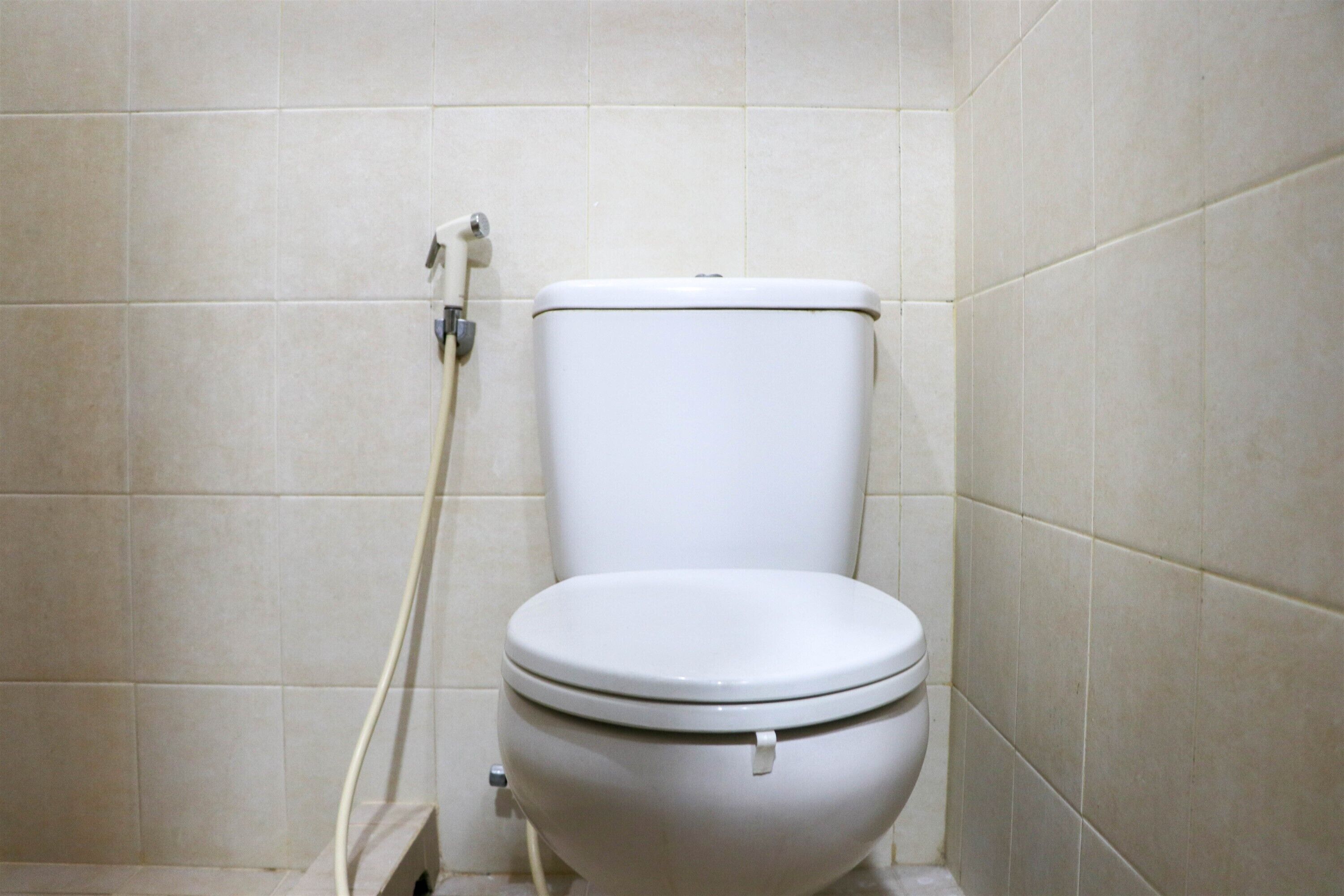 Eine weiße Standardtoilette in einem Badezimmer mit beige farbenen Fliesen.