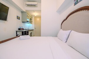 Quarto de hotel com cama, escrivaninha com computador e cozinha compacta.
