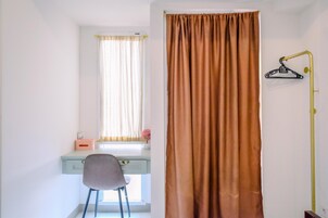 Quarto com escrivaninha, cadeira e janela com cortinas.