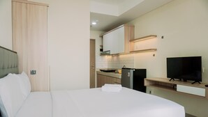 A hotel room with a bed, a TV, a kitchen area, and a wooden wardrobe. - Homey Living And Comfy Studio Apartment At B Residence (Pagedangan)