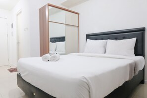 A neatly made bed with white linens, a dark headboard, and two rolled towels on the foot of the bed.