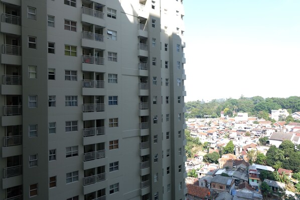A high-rise building with multiple balconies and a view of a densely populated area with various buildings and greenery in the background.
