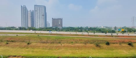 A cityscape with high-rise buildings, a highway, and green fields.