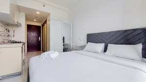 A hotel room with a large bed, a wardrobe, a small table, and a kitchen area. - Fully Furnished With Cozy Studio Sky House Bsd Apartment (Pagedangan)