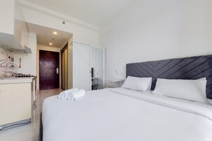 Quarto de hotel com uma cama grande, um guarda-roupa, uma mesa pequena e uma área de cozinha.