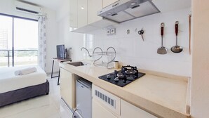 A modern kitchen with a gas stove, sink, and a small refrigerator. There is a window with a view of the outdoors. - Fully Furnished With Cozy Studio Sky House Bsd Apartment (Pagedangan)