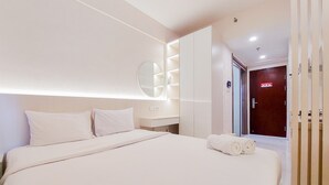 A modern hotel room with a large bed, a bedside table, a mirror, and a wardrobe. - Comfy Designed And Modern Studio At Sky House Bsd Apartment (Pagedangan)