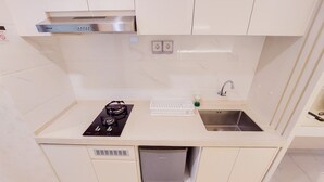 A compact kitchen with a built-in gas stove, a sink, and a compact refrigerator. - Comfy Designed And Modern Studio At Sky House Bsd Apartment (Pagedangan)