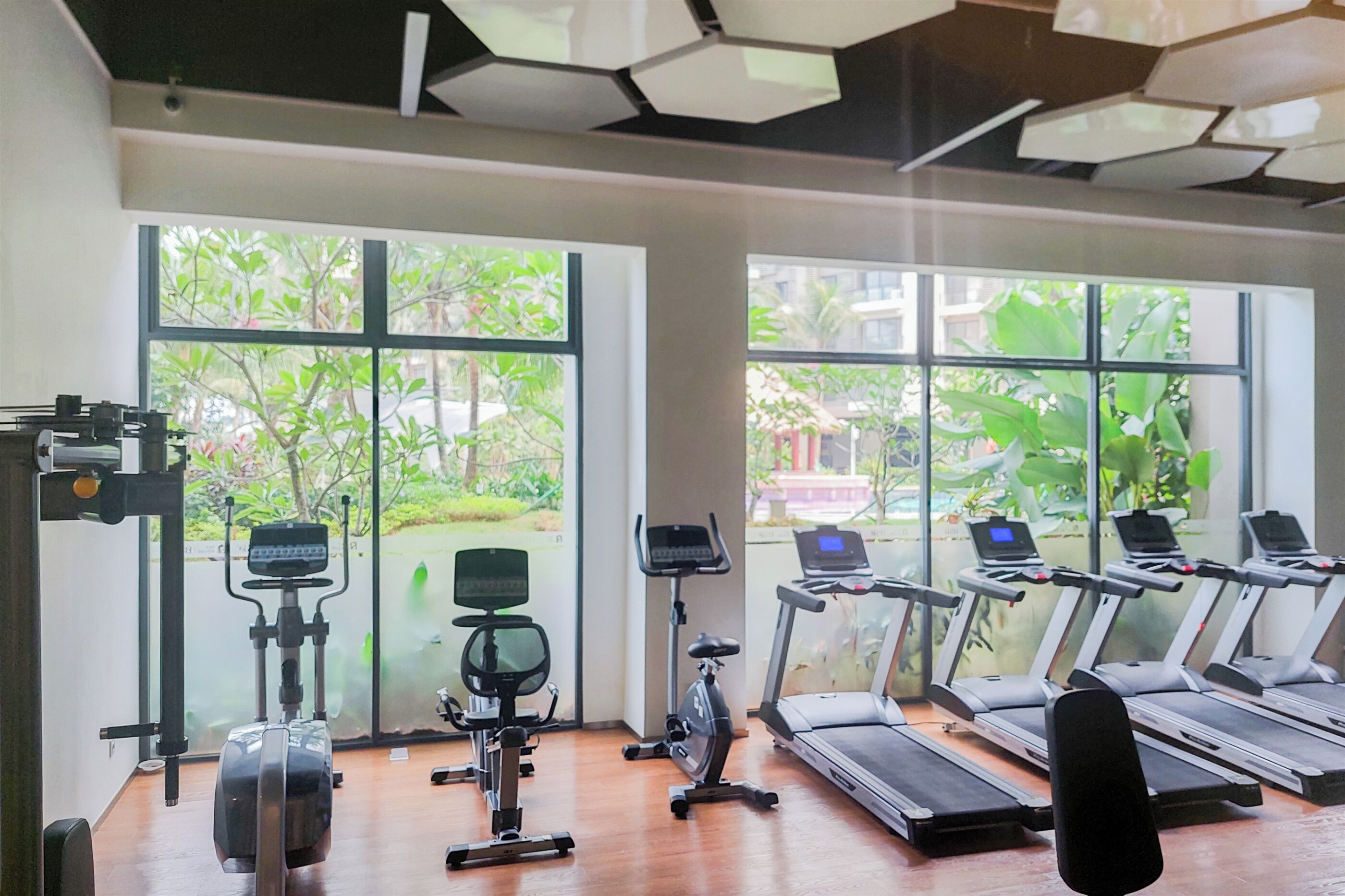 A gym with exercise equipment, large windows, and a view of greenery.