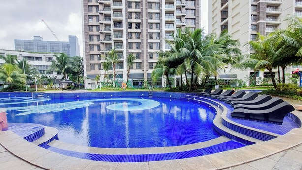 A large outdoor swimming pool with a blue tiled design, surrounded by lounge chairs and palm trees. - Warm And Nice Studio Room Sky House Bsd Apartment (Pagedangan)
