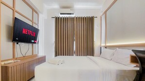 A hotel room with a bed, a TV displaying 'NETFLIX', a wooden bedside table, and a window with curtains. - Warm And Nice Studio Room Sky House Bsd Apartment (Pagedangan)