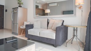 Ein modernes Wohnzimmer mit einem grauen Sofa, einem kleinen runden Tisch, einem Kühlschrank und einem großen Spiegel an der Wand.