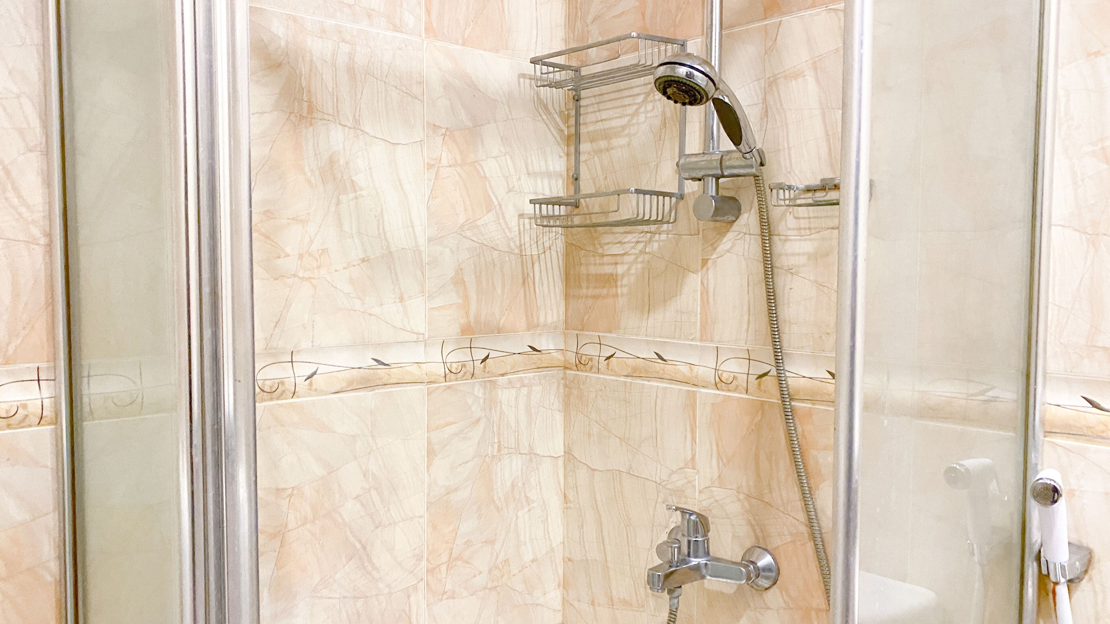 A glass-enclosed shower with a handheld showerhead and a wall-mounted faucet.