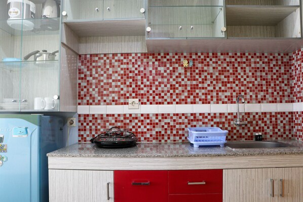 Une cuisine avec un crédence à carreaux rouges et blancs, un réfrigérateur bleu et un évier.