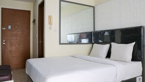 A hotel room with a large bed, a wooden door, a mirror, and a wall-mounted phone. - Compact And Elegant Studio Maple Park Sunter Apartment (Jakarta)