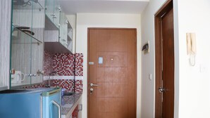 A compact kitchen with a blue refrigerator, a wooden door, and a red and white tiled backsplash. - Compact And Elegant Studio Maple Park Sunter Apartment (Jakarta)
