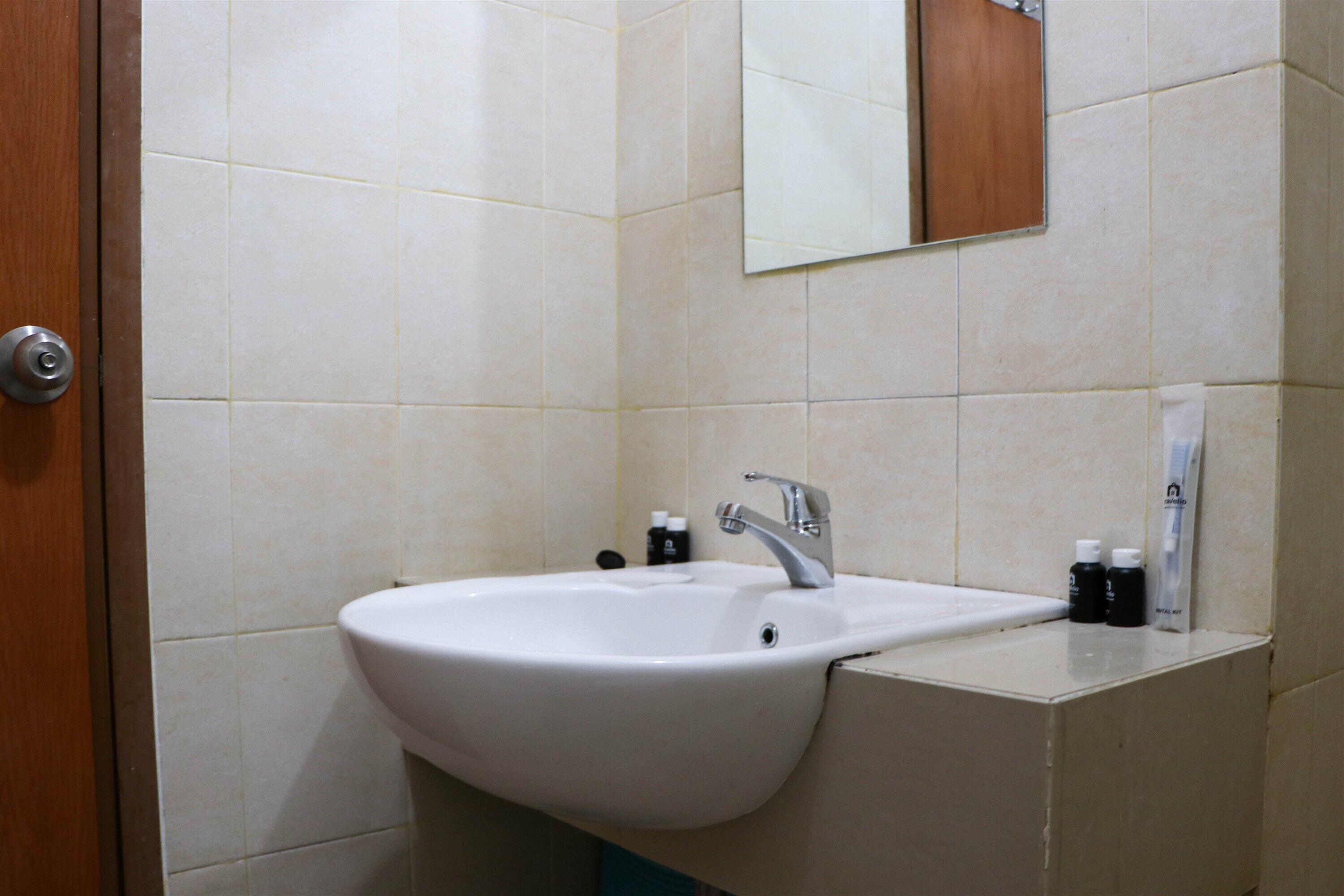 Un baño con lavamanos blanco, un espejo y artículos de aseo en la encimera.