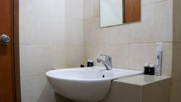 Un baño con lavamanos blanco, un espejo y artículos de aseo en la encimera.
