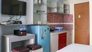 A compact kitchen with a flat-screen TV, a blue refrigerator, and a red door. - Compact And Elegant Studio Maple Park Sunter Apartment (Jakarta)