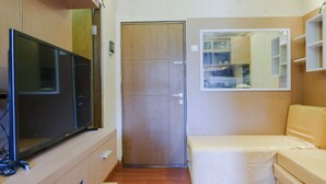 Ein kompakter Wohnraum mit Fernseher auf einem Holzschrank, einem beigen Sofa, einer Holztür und einem Spiegel, der den Raum widerspiegelt.