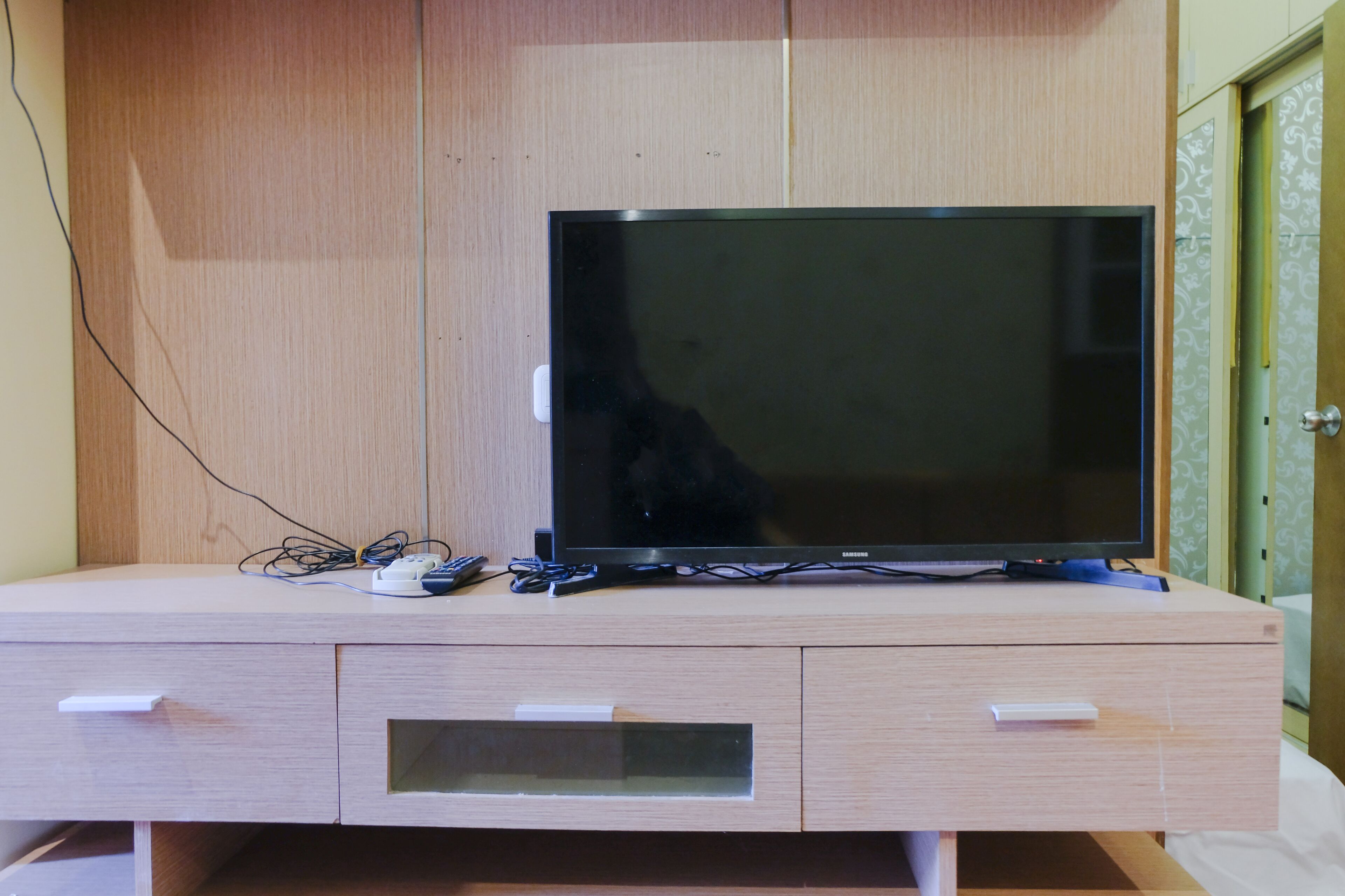 A wooden TV stand with a flat-screen TV, a power strip, and a remote control.