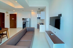 A modern living room with a sofa, a dining table, a kitchen area, and a TV mounted on the wall.