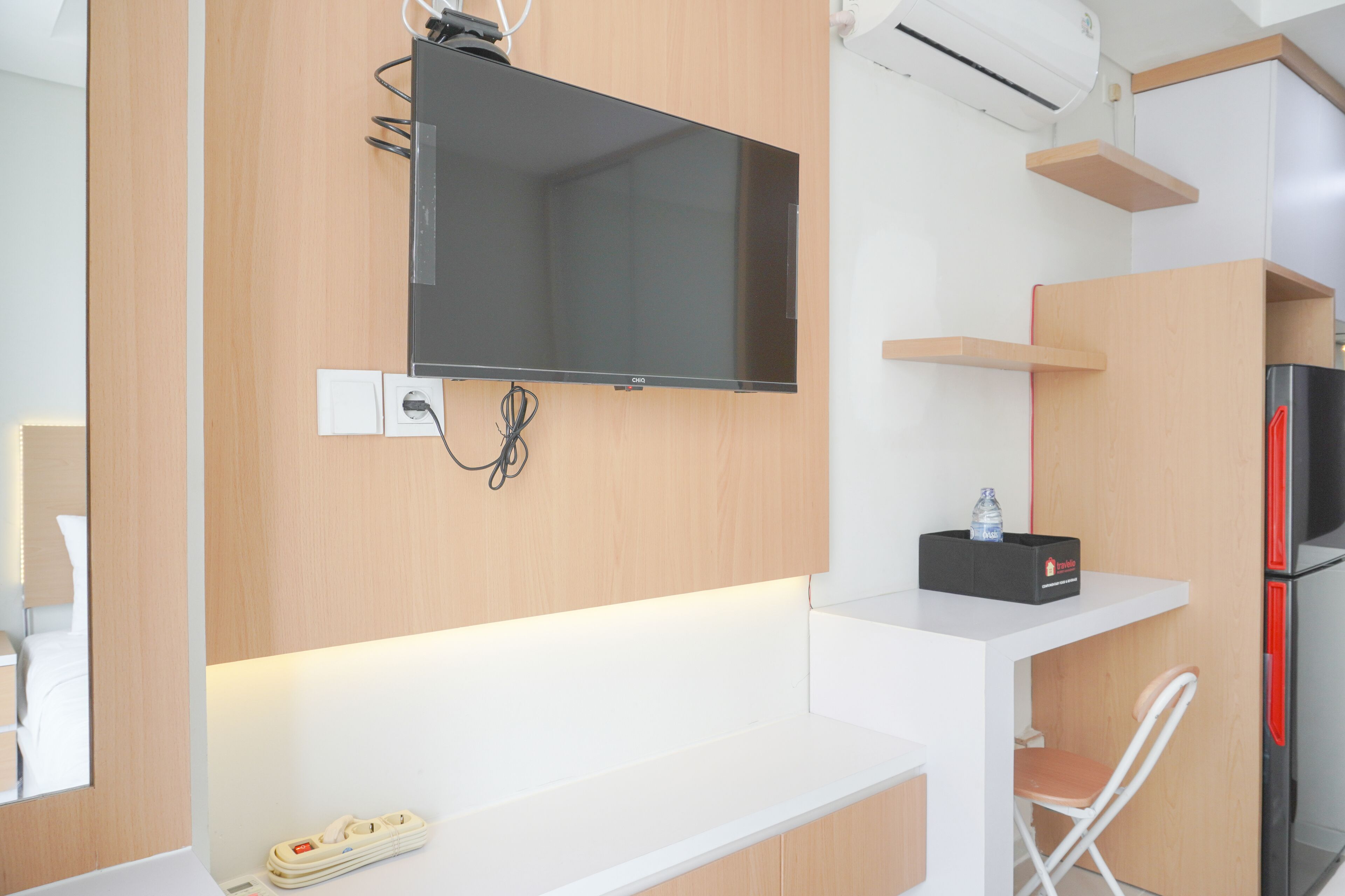 Una cocina moderna con una televisión de pantalla plana sobre una encimera blanca, un refrigerador empotrado y armarios de madera.