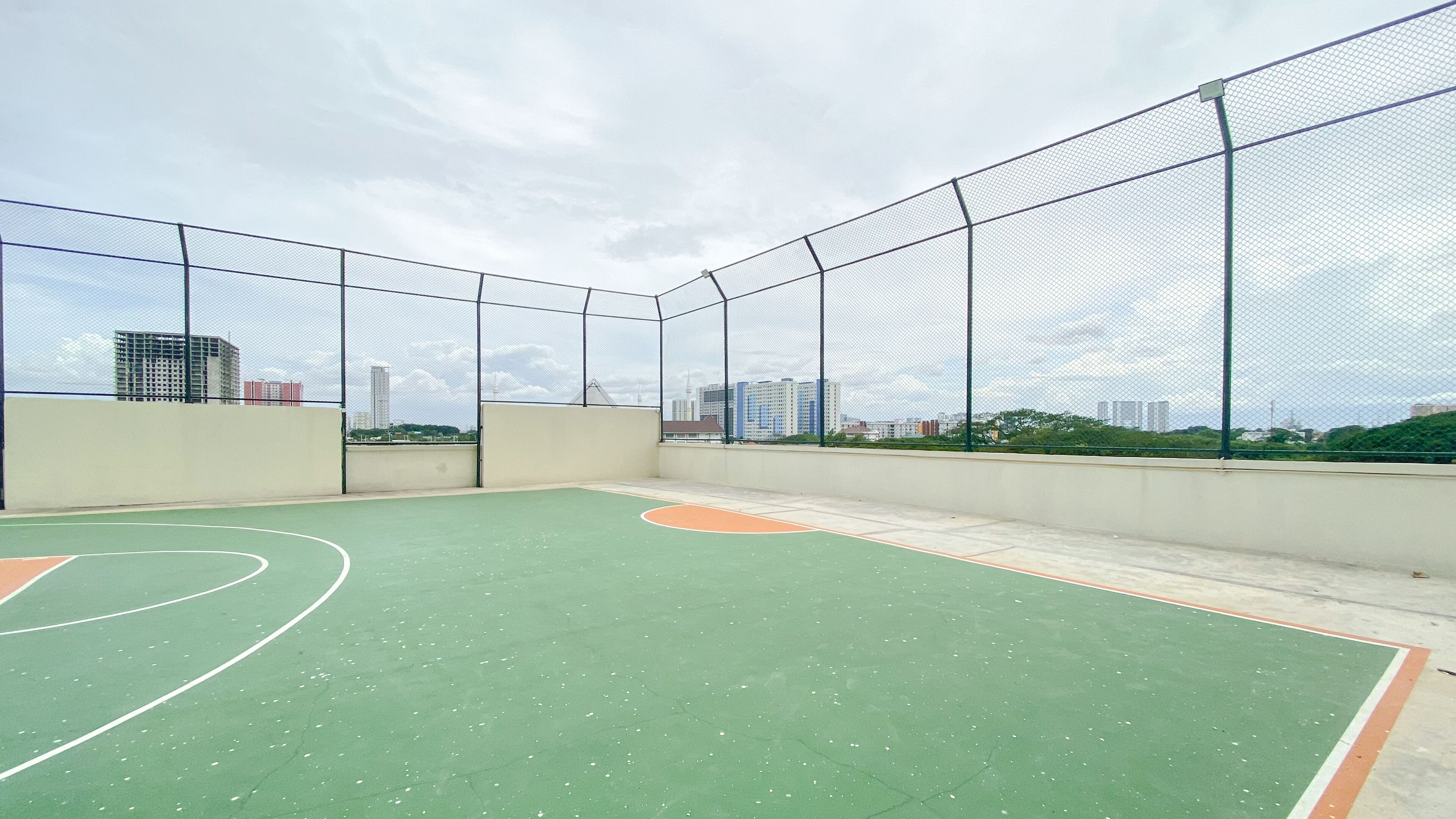 An outdoor basketball court with a cityscape view, surrounded by a mesh fence.