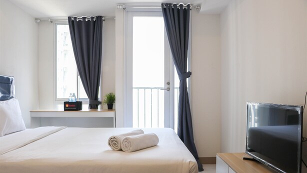 A hotel room with a bed, a TV, a desk with a computer, and a window with curtains. - Brand New Studio At Tokyo Riverside Pik 2 Apartment (Teluknaga)